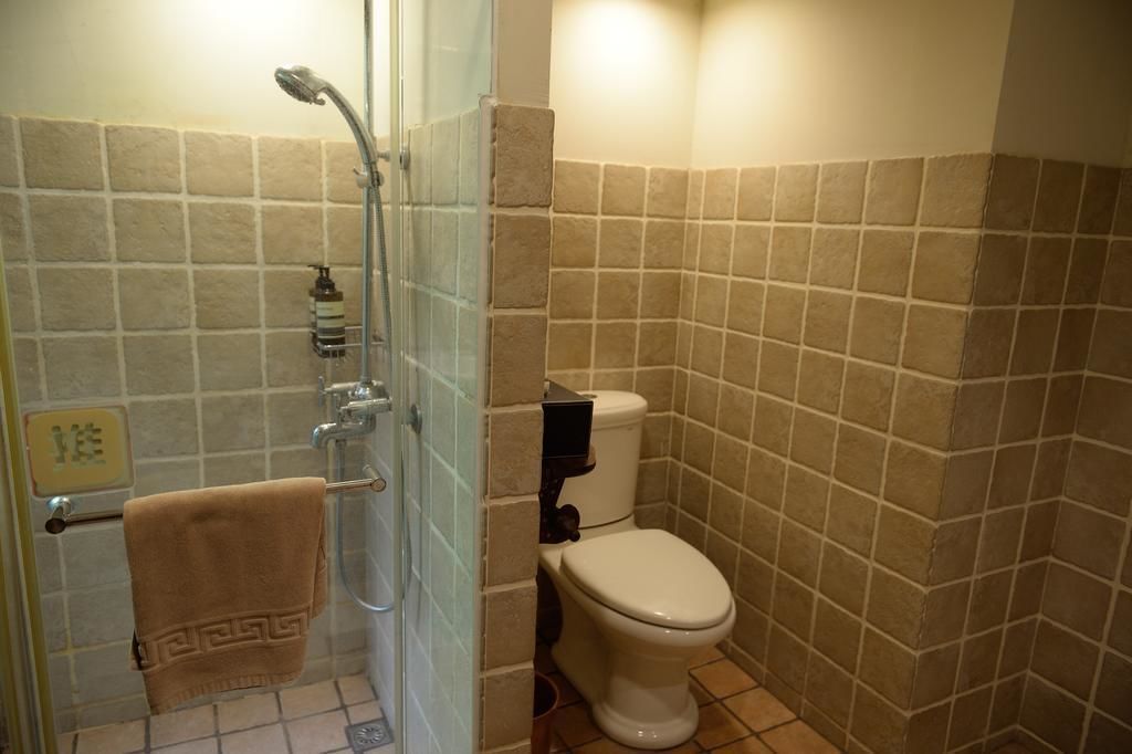 A bathroom with a glass-enclosed shower, a toilet, and beige tiled walls.