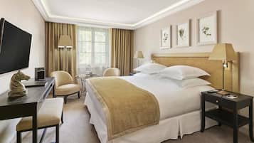 A hotel room with a bed, two chairs, a desk with a TV, a lamp, and framed pictures on the wall.