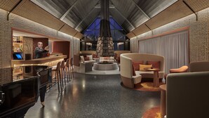 A modern hotel lobby with a high ceiling, a central seating area, and a bar with a bartender. - Château Saint-Jean (Montlucon)