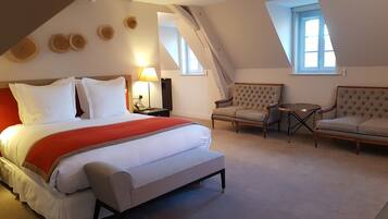A bedroom with a large bed, a chair, a small table, and a lamp.