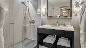 Un baño moderno con ducha envuelta en vidrio, un lavamanos con espejo y toallas ordenadas sobre la encimera.