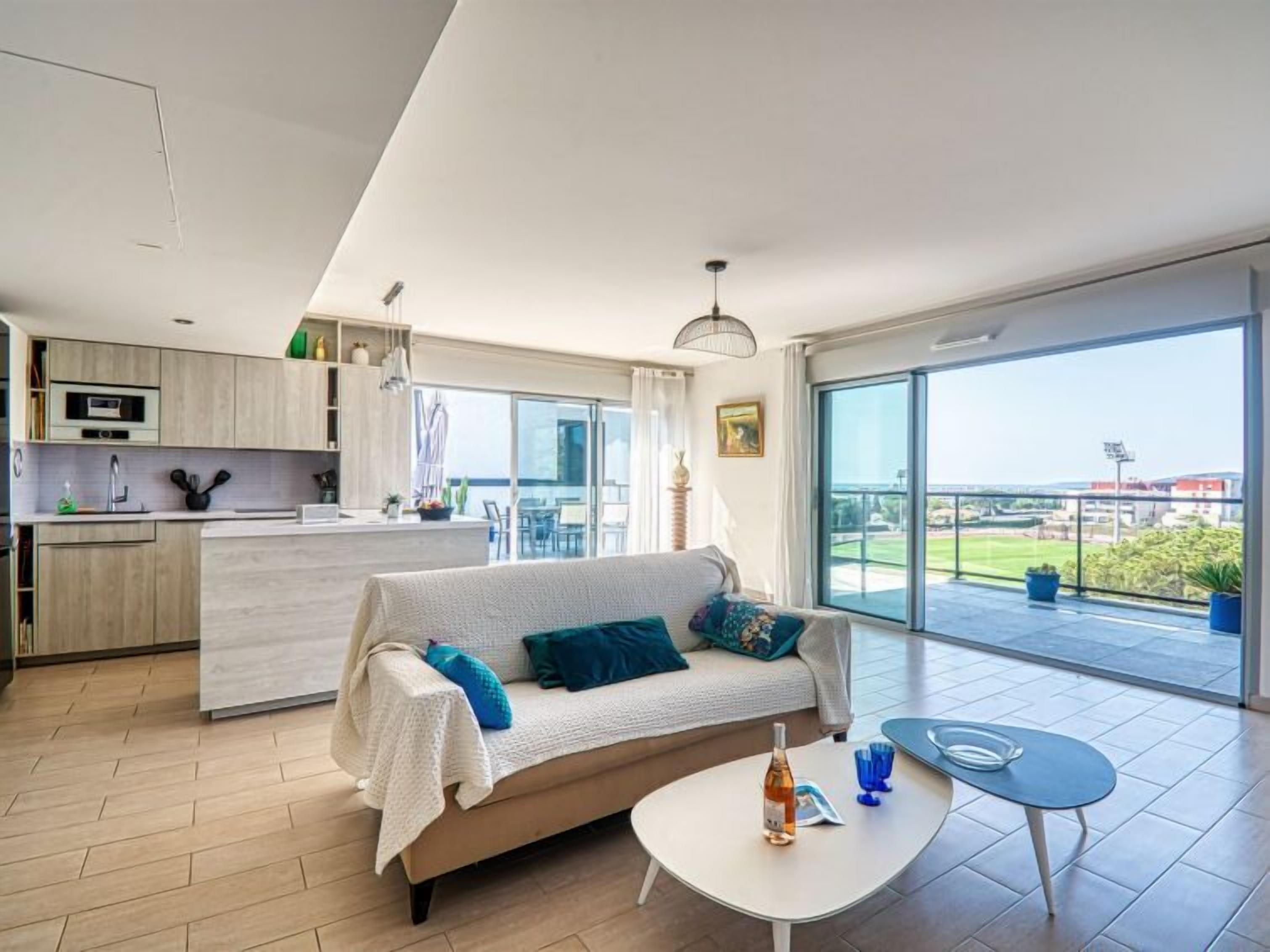 A modern apartment with a living area, kitchen, and balcony with a view.