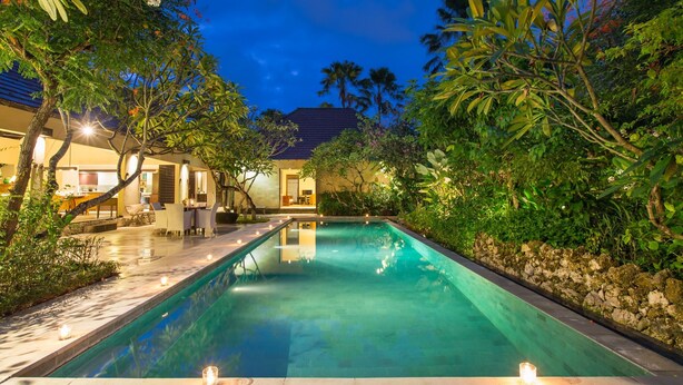 A swimming pool surrounded by lush greenery and a well-lit outdoor area with a stone wall and a building in the background. - 3 Bedroom Balinese Style Villa, Lovely Villa Close to Shopping Area Seminyak (Seminyak)