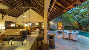 A spacious indoor area with a high ceiling, a dining area with a poolside view, and a kitchen area with bar seating. - 3 Bedroom Balinese Style Villa, Lovely Villa Close to Shopping Area Seminyak (Seminyak)