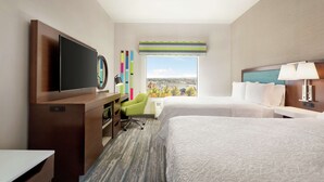 Une chambre d’hôtel avec deux lits, un bureau avec une chaise, une télévision et une fenêtre donnant sur la ville.