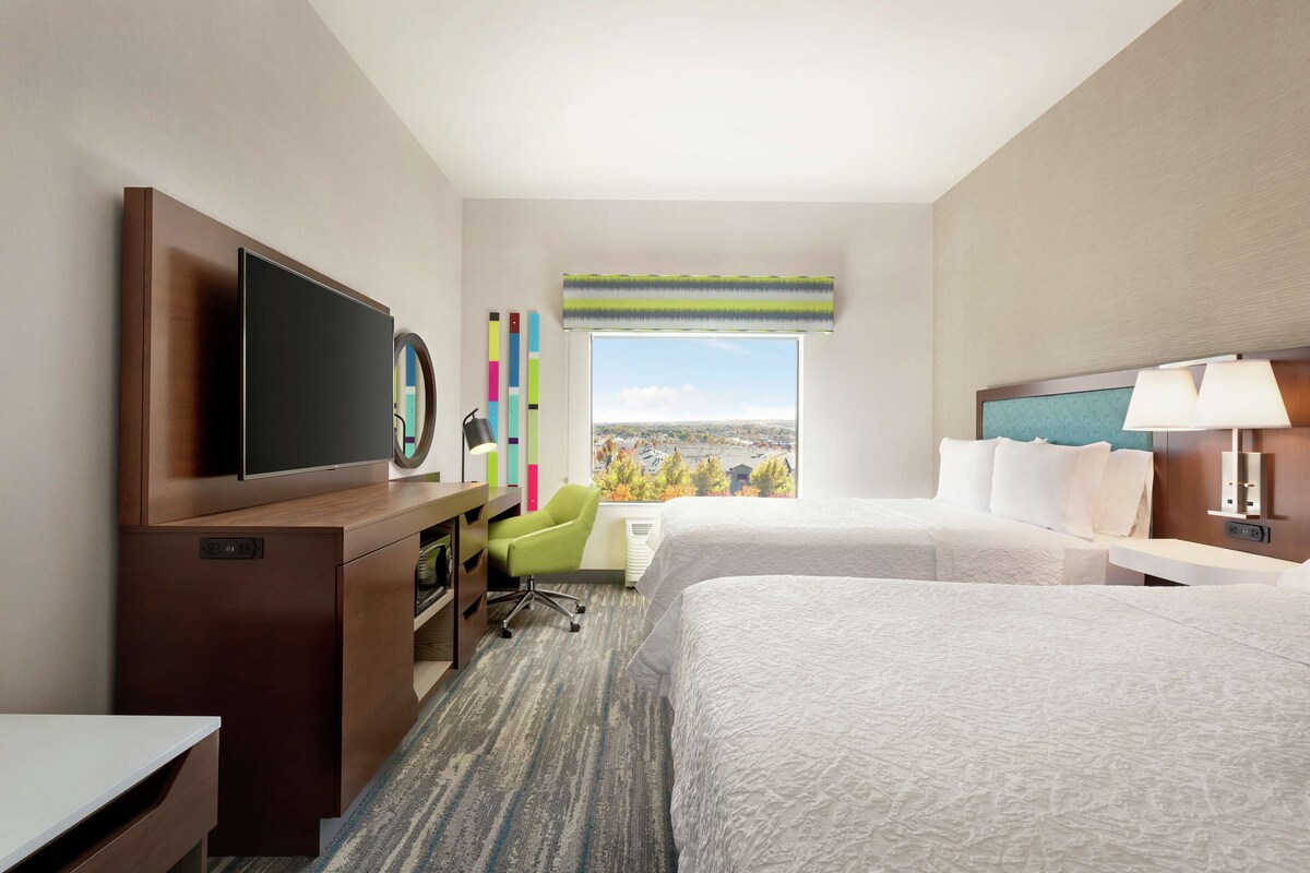 Une chambre d’hôtel avec deux lits, un bureau avec une chaise, une télévision et une fenêtre donnant sur la ville.