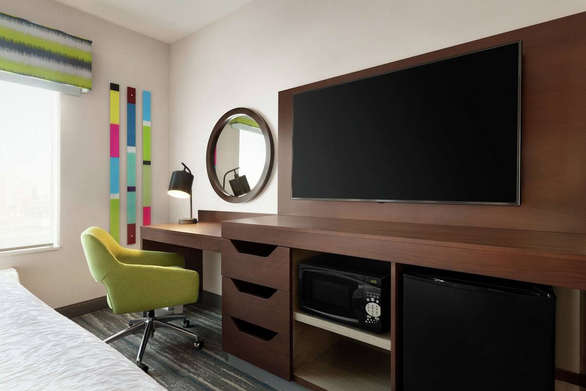 Une chambre d’hôtel équipée d’un lit, d’un bureau avec une chaise, d’un téléviseur à écran plat, d’un four à micro-ondes et d’un réfrigérateur.