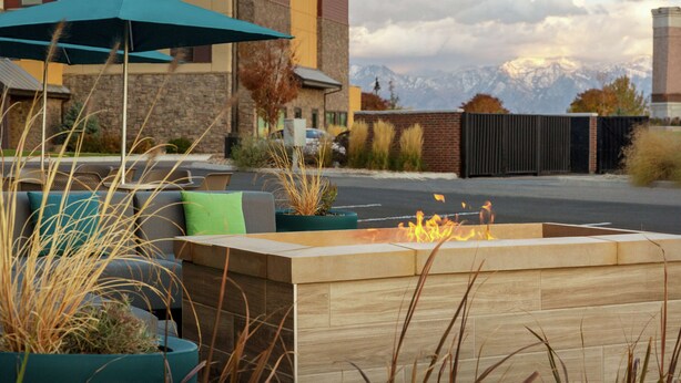 Un espace extérieur moderne aménagé avec des sièges, doté d’un foyer, entouré de plantes en pot et offrant une vue sur les montagnes.