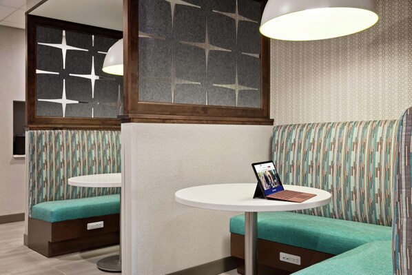 Un espace détente avec une tablette posée sur une petite table, des bancs rembourrés et un mur décoré de motifs.