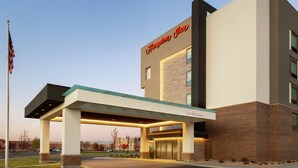 Un hôtel moderne, reconnaissable à son grand panneau « Hampton Inn », doté d’une entrée abritée et d’un espace pelouse bien entretenu.