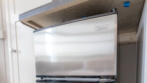 A stainless steel refrigerator in a kitchen with a light wood floor and white cabinetry.