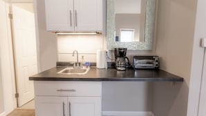 A small kitchen with white cabinets, a black countertop, a coffee maker, a toaster, and a mirror.