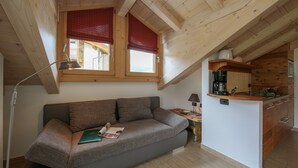 Una habitación estilo loft acogedora con sofá integrado, una pequeña zona de cocina y un ventanal con persianas rojas.