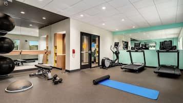 Ein Fitnessraum mit Trainingsgeräten, einer blauen Matte und einem Laufband.