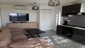 A modern living room with a sofa, a flat-screen TV, and a dining area with a kitchen. - Apartment with pool and magnificent views in the South of France (Saint-Chamas)