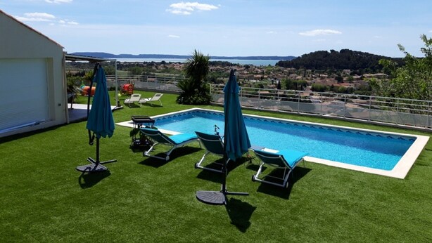 A swimming pool with artificial grass, lounge chairs, and umbrellas. - Apartment with pool and magnificent views in the South of France (Saint-Chamas)