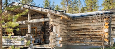 A log cabin with a stone foundation, wooden steps leading to the entrance, and a snow-covered ground.