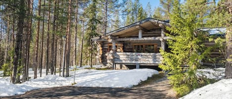 Una baita di legno con un portico coperto, circondata da alti pini innevati.