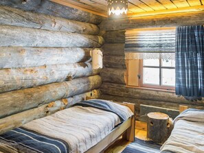A log cabin room with two beds, a window with curtains, and a hanging light fixture.
