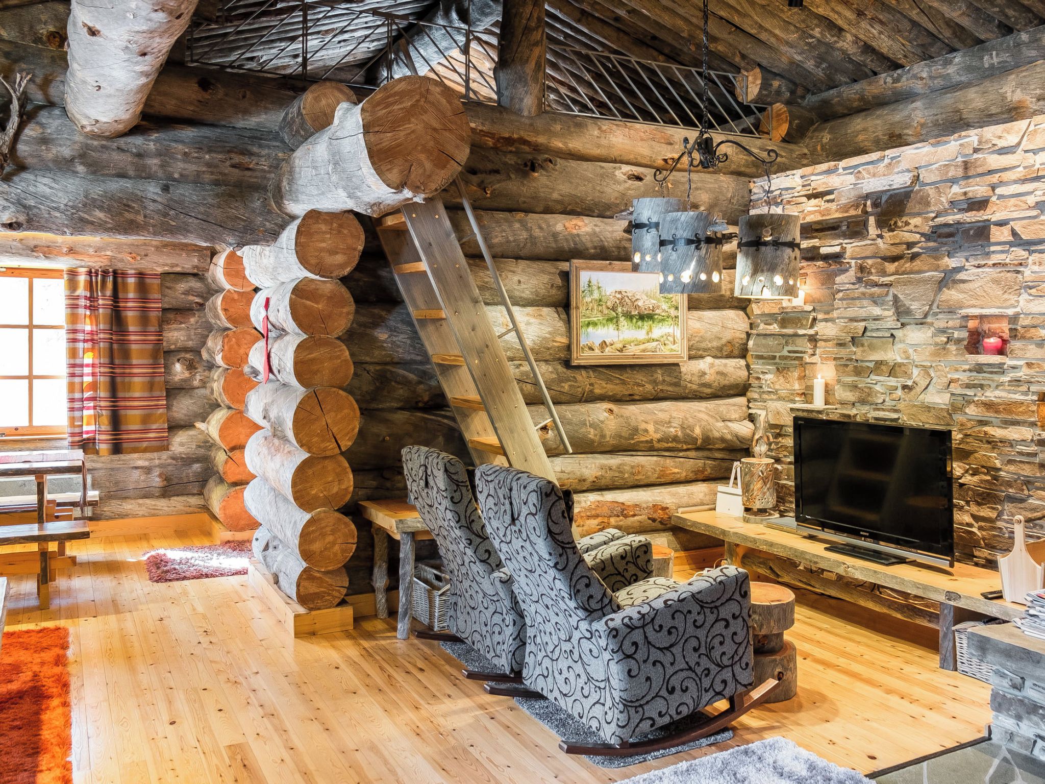 A log cabin interior with a stone wall, wooden furniture, and a television.