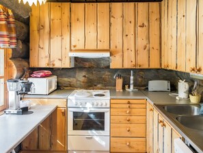A kitchen with wooden cabinets, a stove, a microwave, and a toaster. - Suutarinkolo by Interhome (Kittilä)