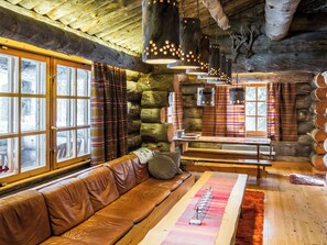 Interior de cabana de madeira com um banco, uma mesa e cortinas xadrez.