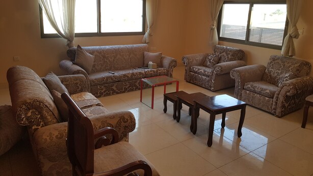 A living room with patterned sofas, a glass coffee table, and a chandelier. - Alburdini (Aqaba)