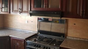 A kitchen with dark wooden cabinets, a stainless steel stove, and a tiled backsplash. - Alburdini (Aqaba)