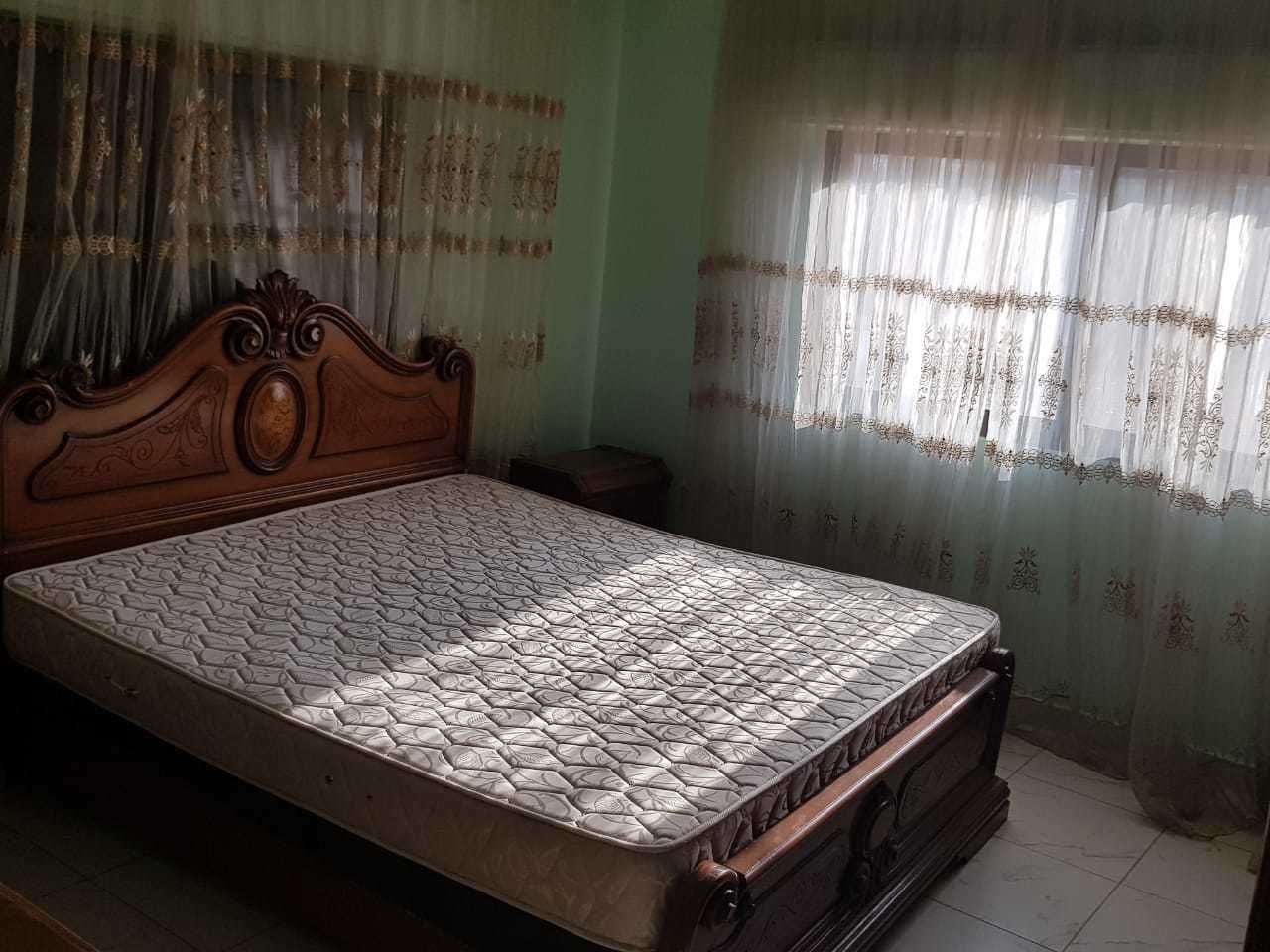 A bedroom with a wooden bed frame, a mattress, and curtains.