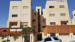 A multi-story building with a central staircase, a car parked in front, and a small tree to the left. - Alburdini (Aqaba)