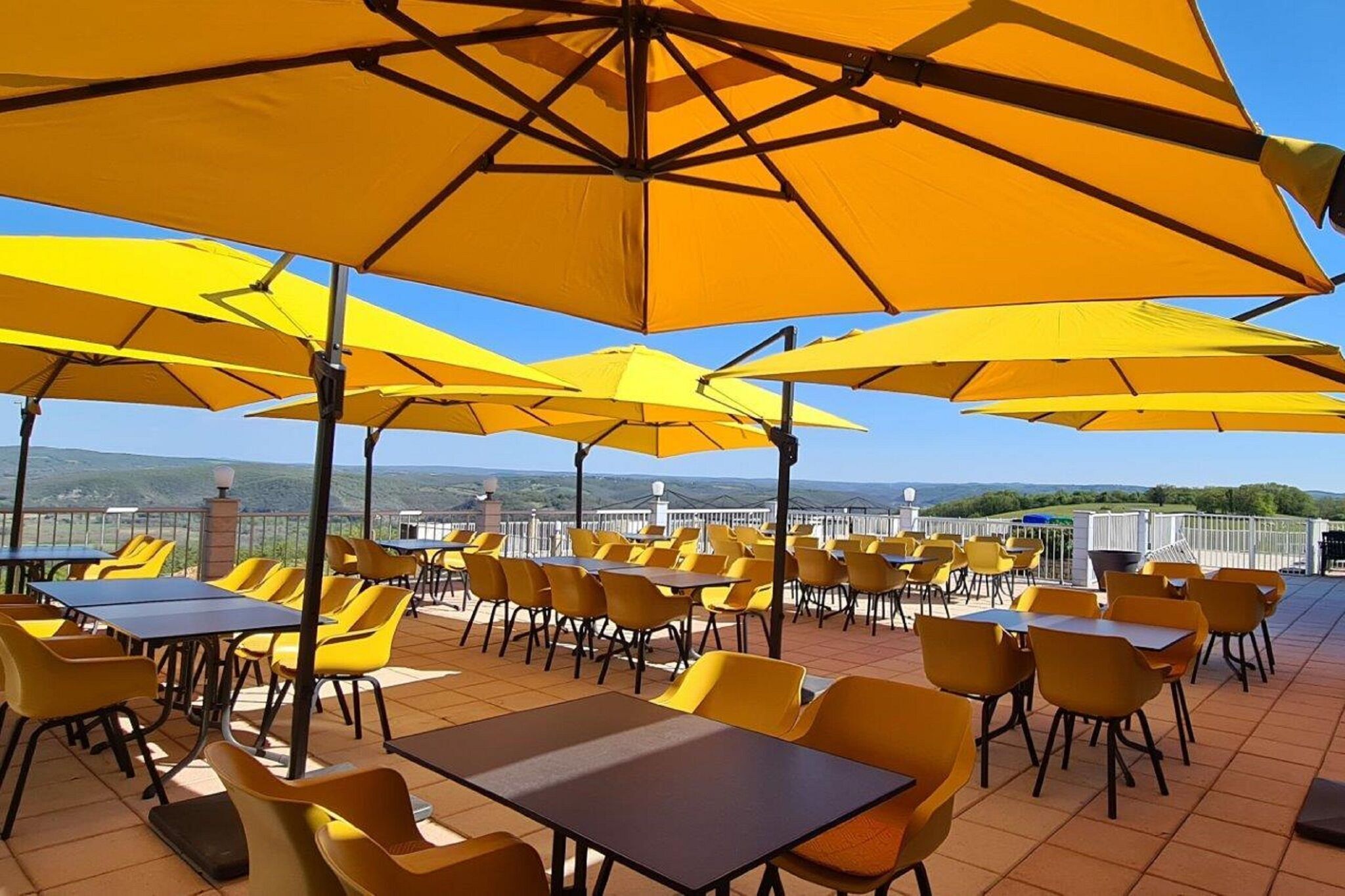 Una terrazza esterna con tavoli e sedie gialli, circondata da grandi ombrelloni gialli.