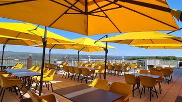 Una terrazza esterna con tavoli e sedie gialli, circondata da grandi ombrelloni gialli.