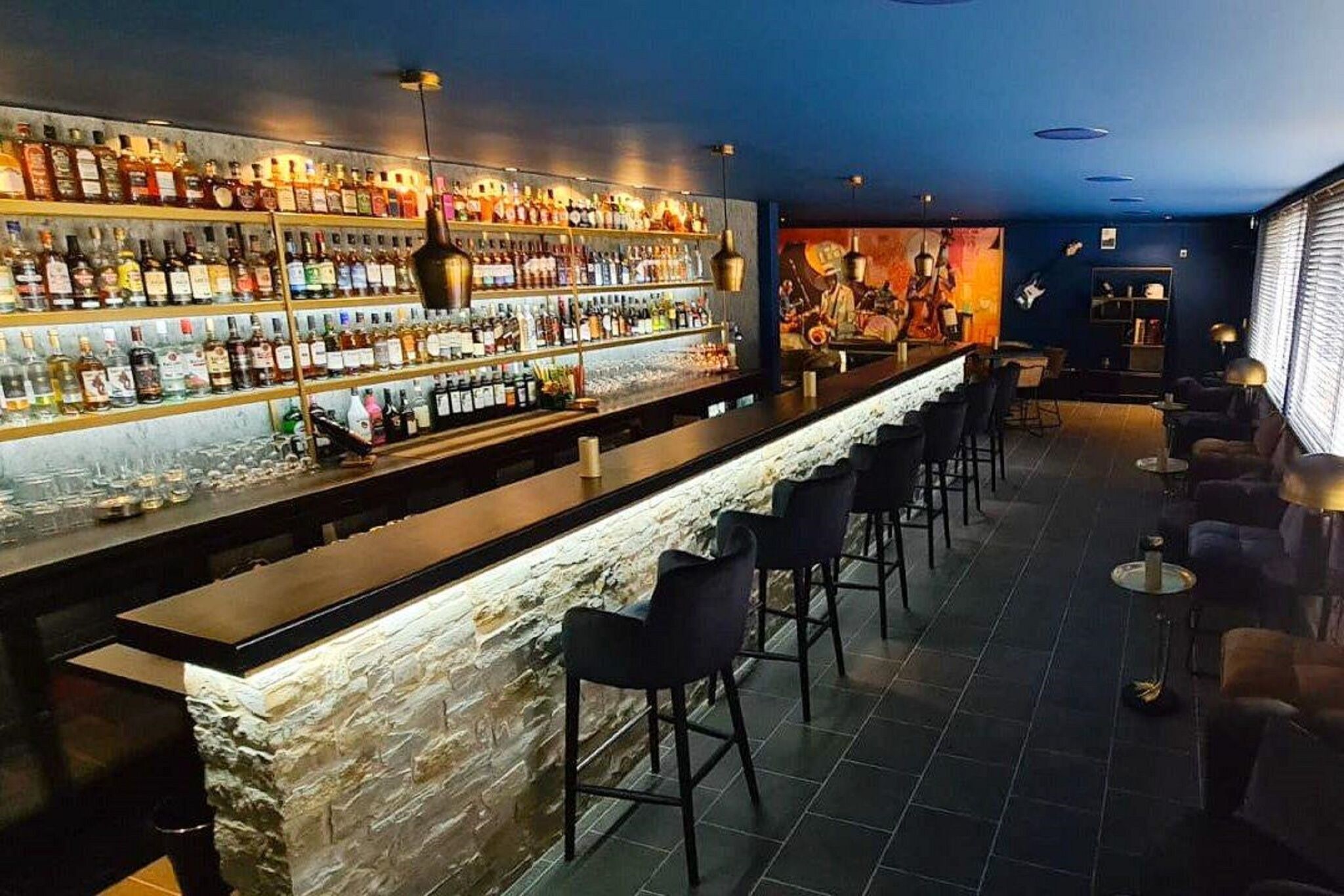 Un'area bar con un bancone in pietra, diverse file di bottiglie di liquori e sgabelli da bar.