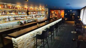 Un'area bar con un bancone in pietra, diverse file di bottiglie di liquori e sgabelli da bar.