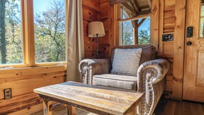Ein gemütliches Blockhaus-Interieur mit einem Holztisch, einem gepolsterten Sessel und einem Fenster mit Blick auf Bäume.