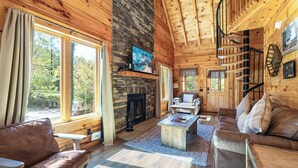 Ein Blockhaus-Interieur mit Kamin, Holzböden, einer Couch, einem Couchtisch und einer Treppe.