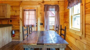 Ein Holzblock-Innenraum mit Esstisch, Stühlen, einer Chandelierleuchtre und Fenstern mit Vorhängen.