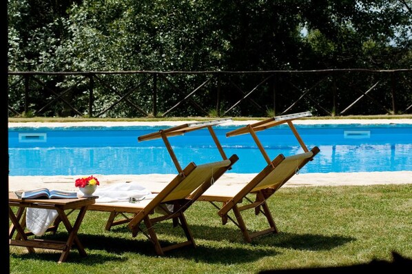 Zona de piscina con sillas de descanso y una mesa con un libro y flores.