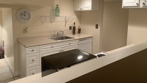 Una cocina con armarios blancos, un lavamanos de acero inoxidable, un reloj y una botella sobre la encimera.