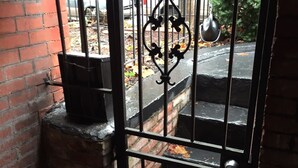 Una reja de metal con una puertecilla decorativa, un muro de ladrillo y una escalera que da al exterior.