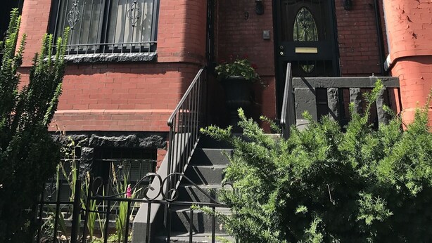 Un edificio de ladrillo rojo de estilo victoriano con puerta frontal negra, ventanas grandes y un pequeño porche.