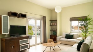 A modern living room with a flat-screen TV, a sofa, a coffee table, and a sliding glass door leading to a balcony. - Amaen Apartment (Chania)