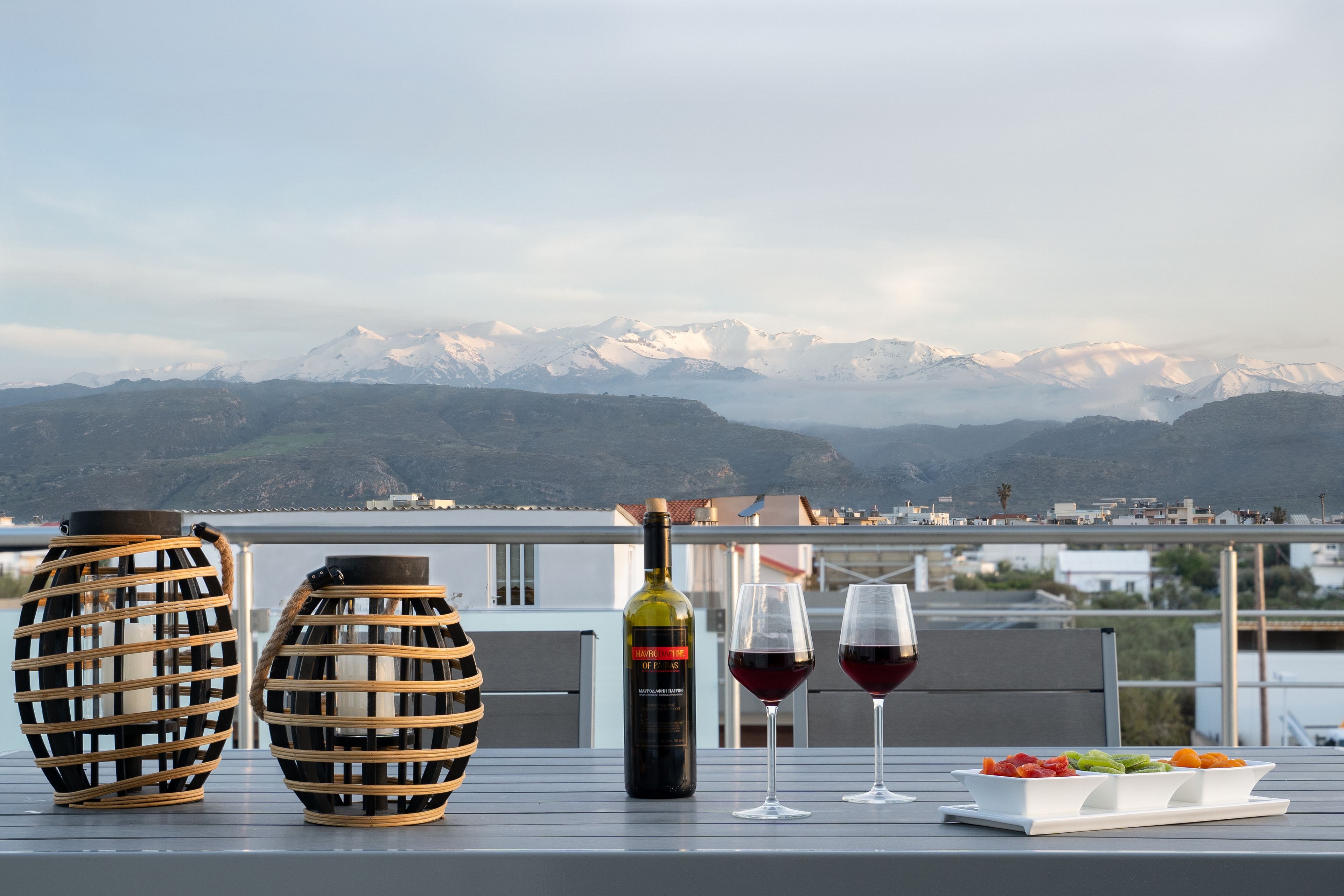 A terrace with two wicker vases, a bottle of wine, two wine glasses, and a plate of fruit.
