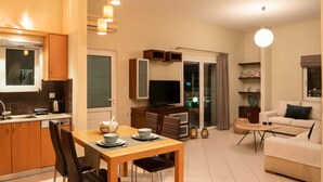 A modern apartment with a kitchen, dining area, and living room. It includes a dining table with chairs, a sofa, a TV, and a coffee machine. - Amaen Apartment (Chania)