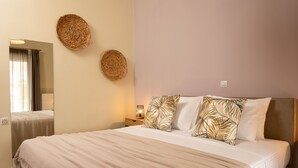 A neatly made bed with a striped blanket, two woven wall decorations, and a bedside table with a lamp. - Amaen Apartment (Chania)