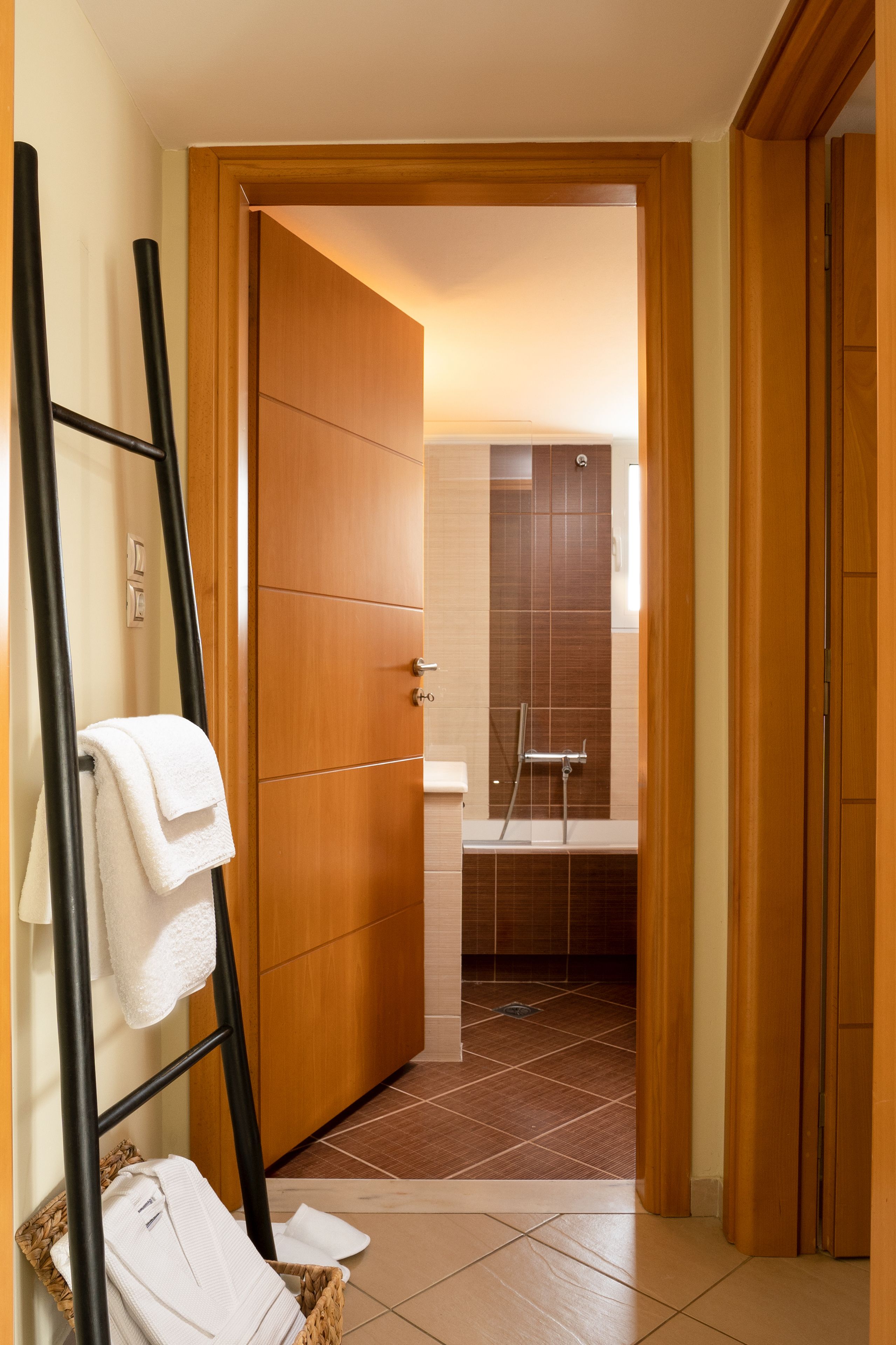 A hallway leading to a bathroom with a shower, a towel rack, and a basket with towels.