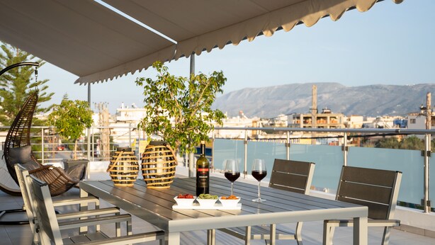 An outdoor dining area with a table set for two, a bottle of wine, and a bowl of fruit. - Amaen Apartment (Chania)