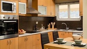 A modern kitchen with wooden cabinets, a microwave, a stove, and a window with a view. - Amaen Apartment (Chania)