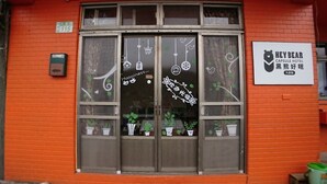 A hotel entrance with a large glass door, potted plants, and a sign for 'Hey Bear Capsule Hotel'. - Hey Bear B&B Jiufen (New Taipei City)