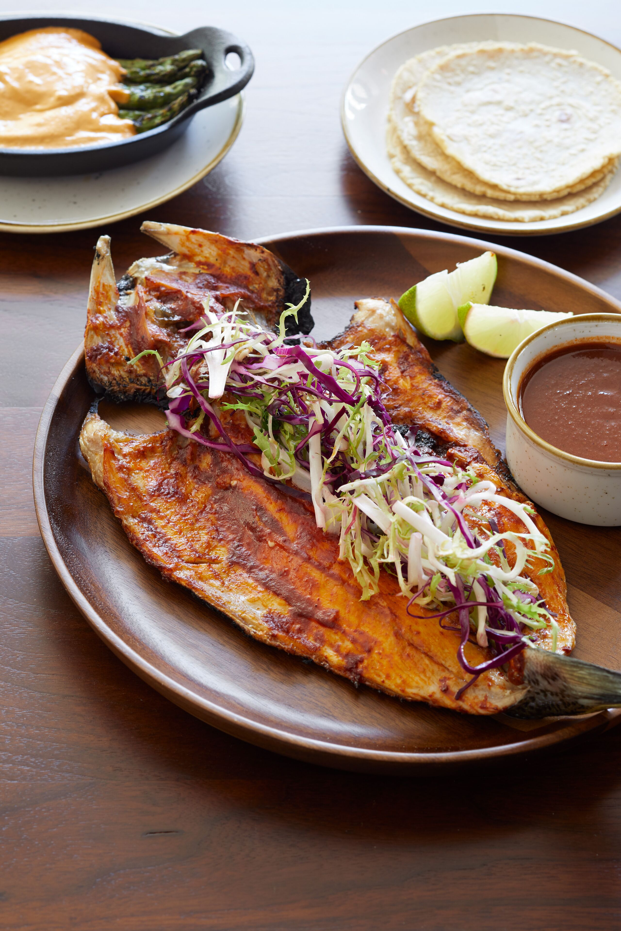 A plate with grilled fish, tortillas, and a side of sauce.